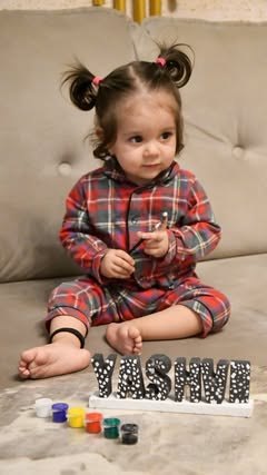Toddler sitting beside a dotted YASHVI name stand and paints